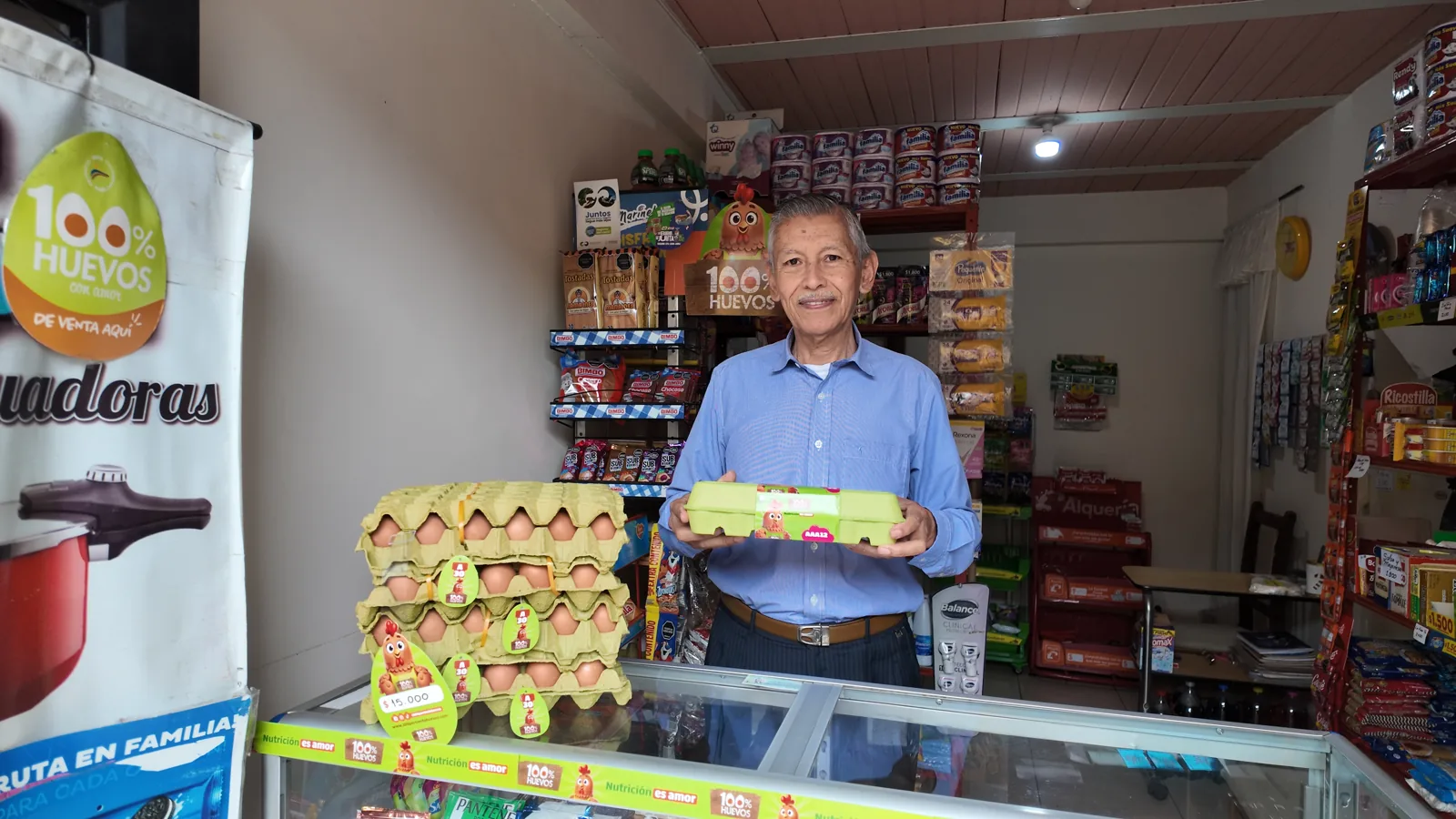 Tendero en su negocio mostrando bandejas de 100% Huevos