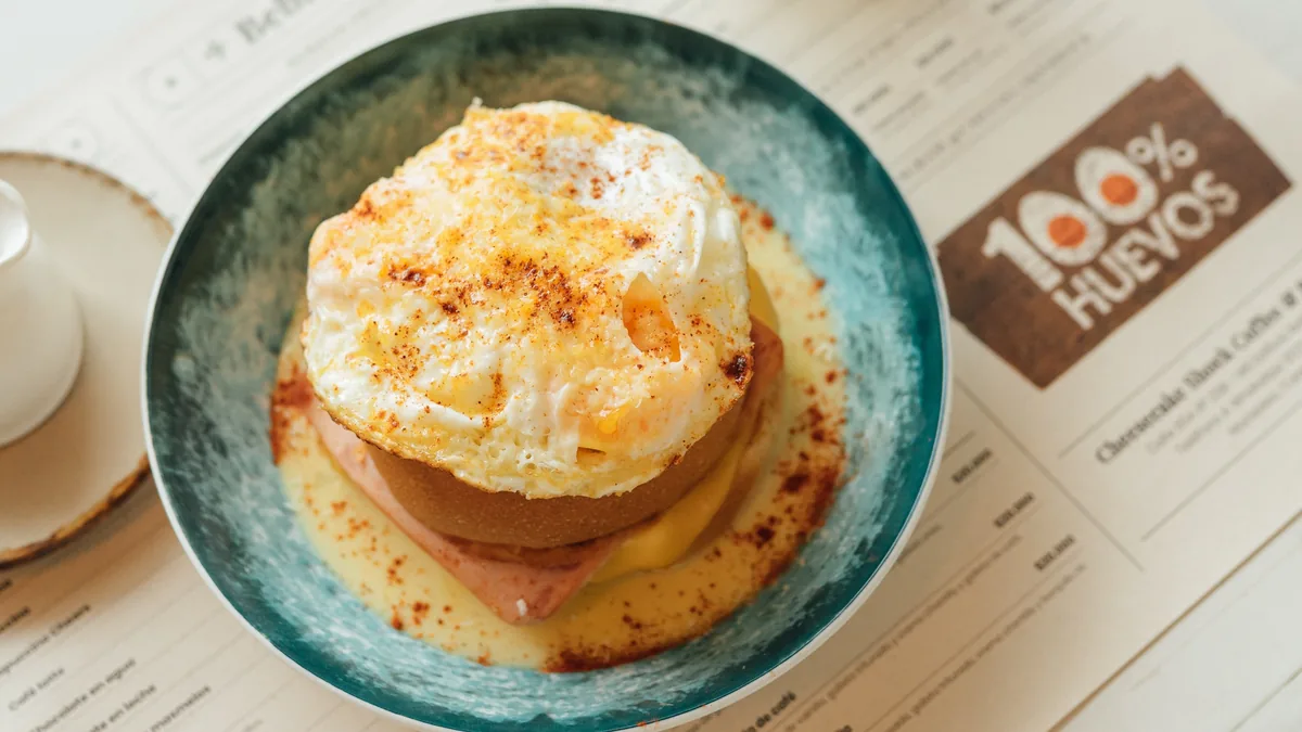 Desayuno preparado con huevo en un plato turquesa, junto a la marca 100% Huevos