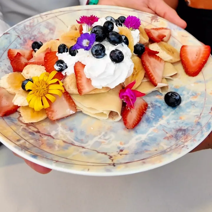 Crepes servidos con crema, fresas, arándanos y flores comestibles