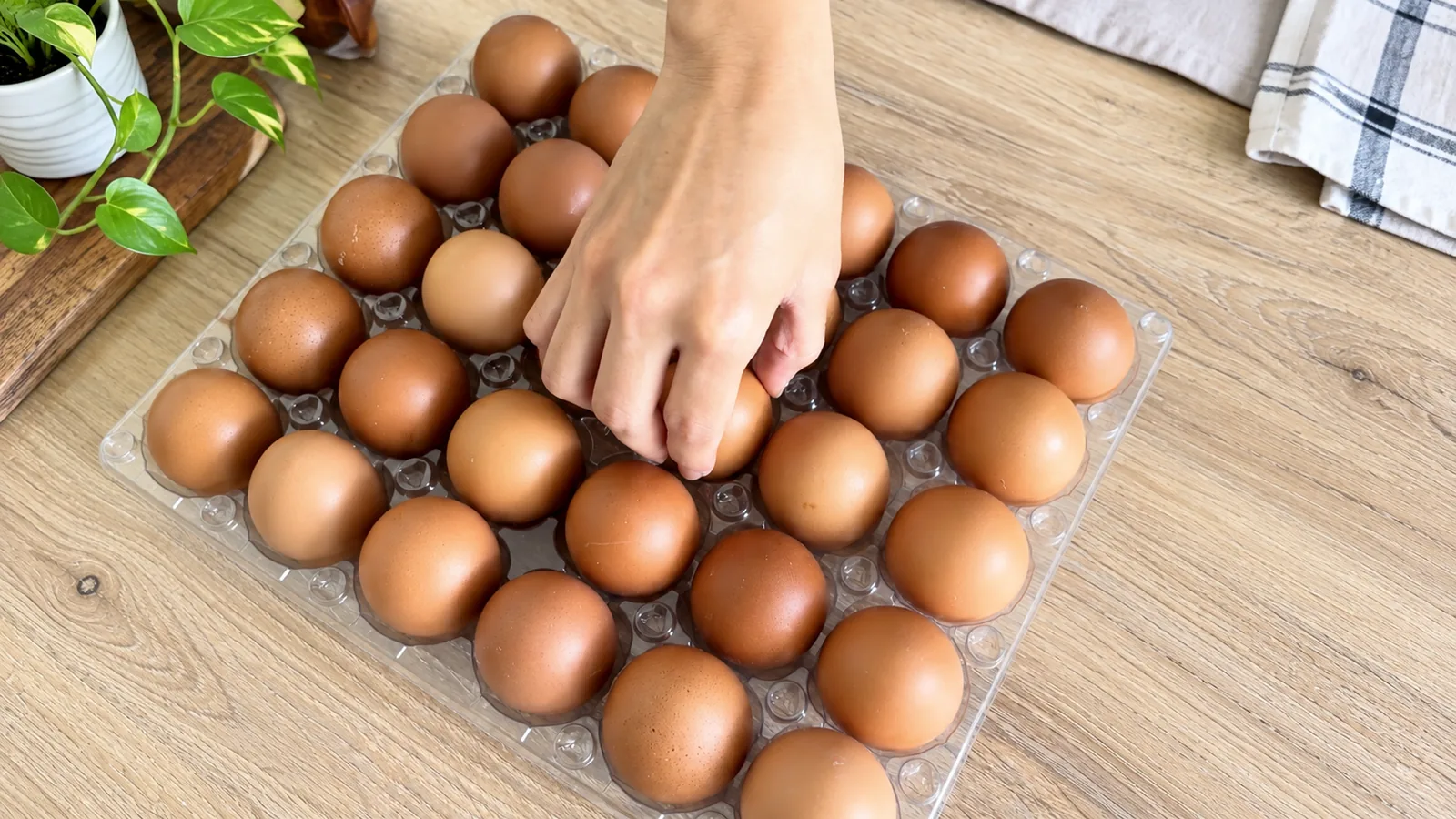 Mano tomando un huevo de una cubeta transparente de 30 sobre una mesa de cocina